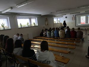 dzieci siedzą na ławkach, policjantka stoi naprzeciwko nich