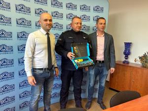 Komendant z nowym analizatorem wydechu w rękach stoi pomiędzy dwoma mężczyznami na tle baneru z napisami WORD.