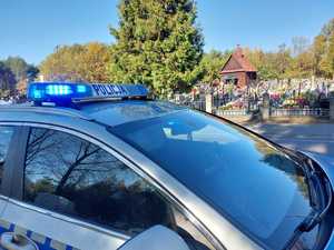 belka z napisem policja na dachu radiowozu w tle widoczny cmentarz.