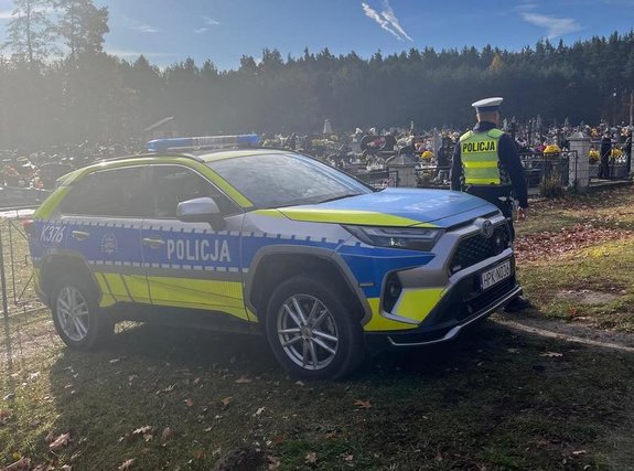 Policjant stoi przed radiowozem przy cmentarzu