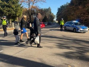 Policjant kieruje ruchem w rejonie cmentarza, policjantka stoi i nadzoruje ruch