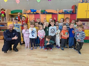 Policjant z najmłodszą grupą dzieci ustawiony do zdjęcia na tle kolorowych szafek