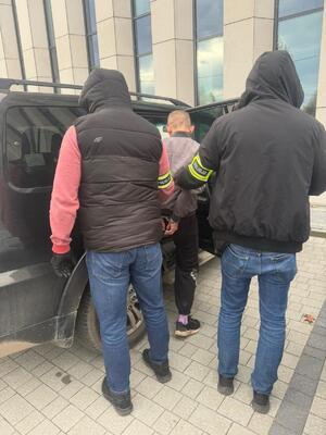 Policjanci prowadzą zatrzymanego mężczyznę do radiowozu