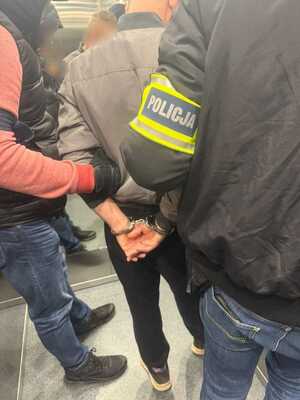 Policjanci trzymają zatrzymanego mężczyznę.