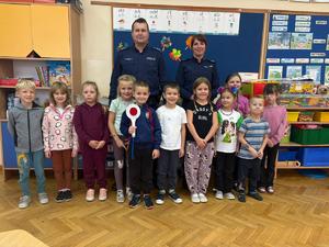 Na tle tablicy stoją policjanci wraz z dziećmi