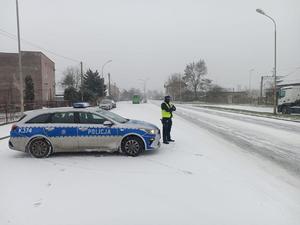 Policjant stoi przy radiowozie na drodze leży śnieg