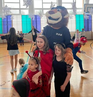 obok policyjnej maskotki lwa stoja dwie dziewczynki