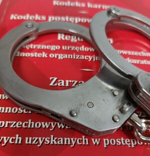 Zdjęcie przedstawia kajdanki policyjne i kodeks karny